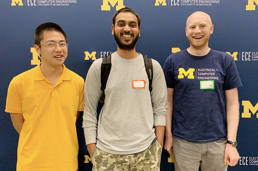 Three guys pose in front of U-M ECE backdrop